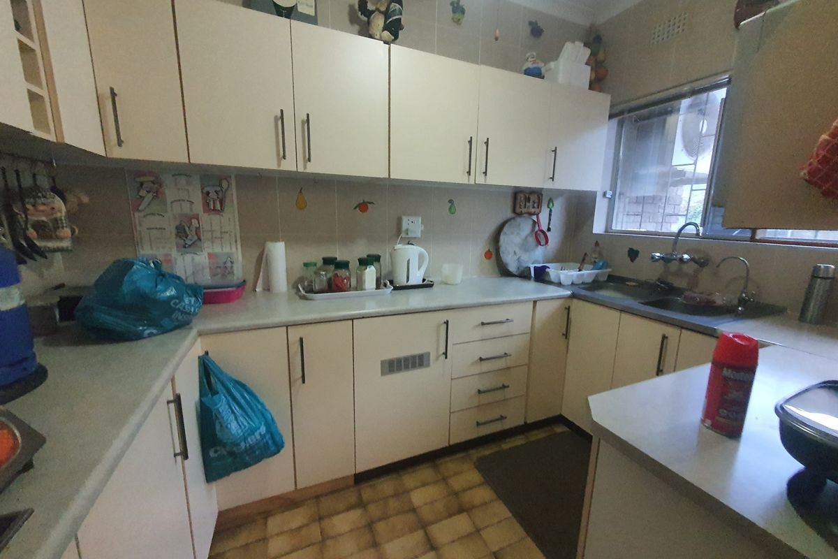 A functional kitchen featuring dated cabinetry, laminate countertops, a double basin sink, and tiled flooring, offering potential for a modern renovation.