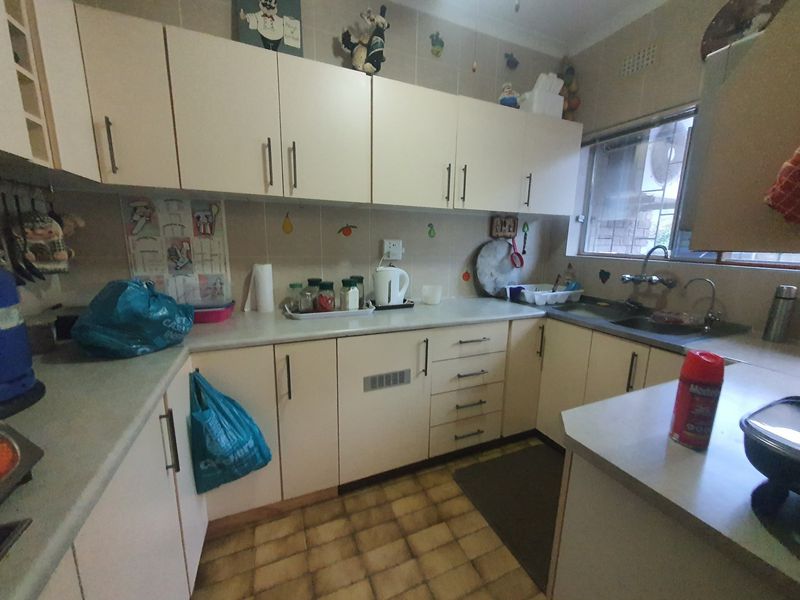 A functional kitchen featuring dated cabinetry, laminate countertops, a double basin sink, and tiled flooring, offering potential for a modern renovation.