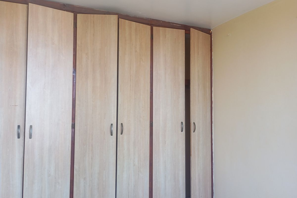 A bedroom featuring dated, built-in wooden cupboards with visible wear and misalignment.