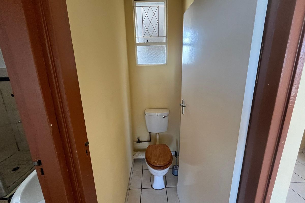A compact, functional guest toilet featuring tiled flooring and a small window with security bars.