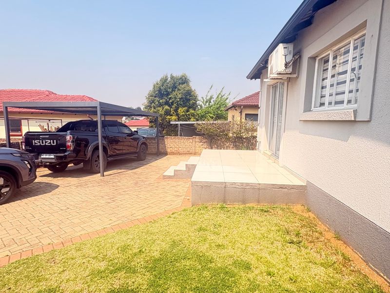 Rear exterior view featuring a paved driveway, carport, and a raised tiled patio area adjacent to the main house structure.