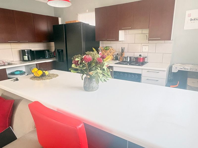 A functional kitchen featuring dark wood cabinetry, white stone countertops, a gas hob, and a central island with breakfast bar seating.