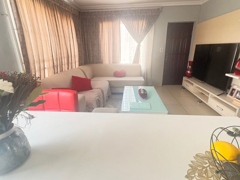 A comfortable living room featuring tiled flooring, cove cornicing, and a built-in media wall unit, offering a functional and well-lit space.