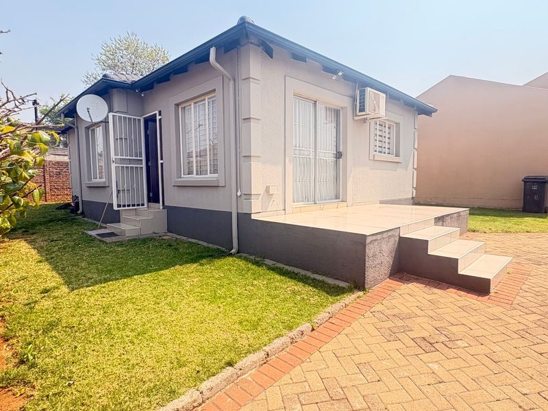 Rear view of the property featuring a tiled patio, paved driveway, and secure access points with an installed air conditioning unit.