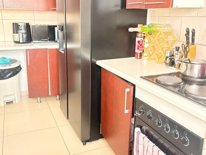 A functional kitchen featuring wood-finish cabinetry, tiled backsplash, electric hob, and built-in oven with tiled flooring throughout.