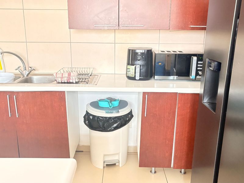 A functional kitchen area featuring laminate cabinetry, a stainless steel double sink, and tiled backsplash with neutral floor tiles.