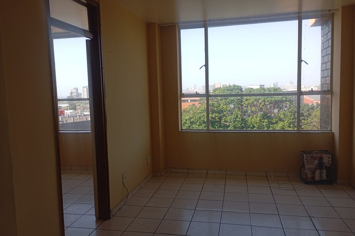 An empty living area featuring tiled flooring and a large window with urban views, offering a blank canvas for interior design.