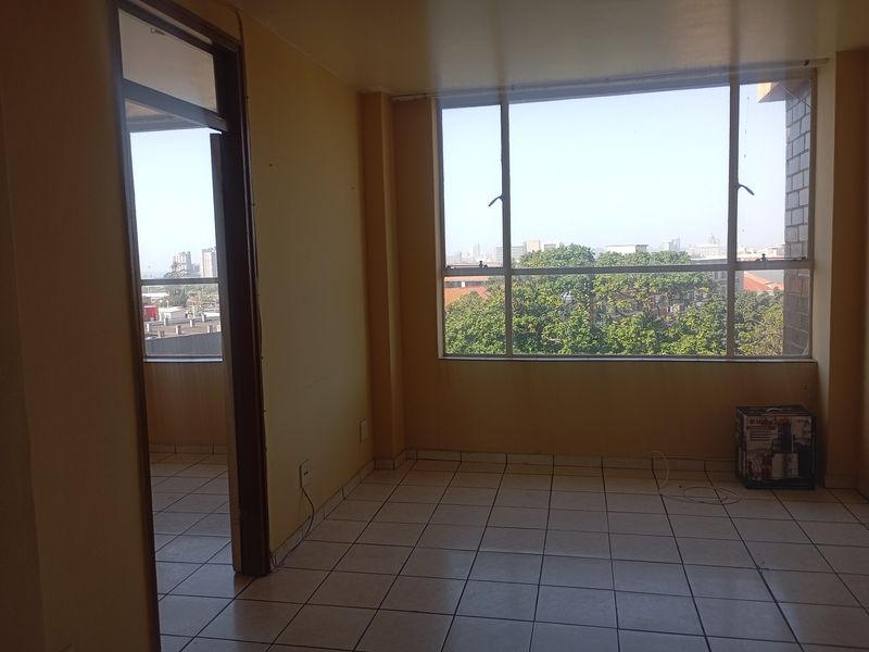 An empty living area featuring tiled flooring and a large window with urban views, offering a blank canvas for interior design.