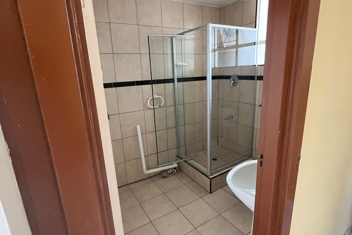A compact bathroom featuring a shower enclosure and pedestal basin, requiring cosmetic updates and finishing of exposed plumbing and ducting.