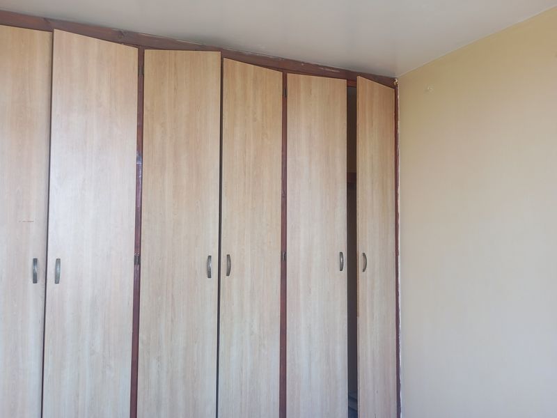 A bedroom featuring dated, built-in wooden cupboards with visible wear and misalignment.