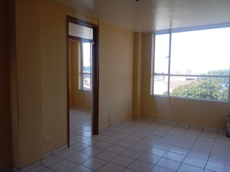 An empty living room featuring tiled flooring, large windows providing natural light, and a doorway leading to an adjacent room.