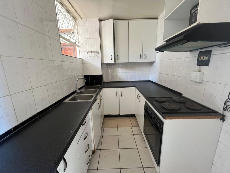 A functional galley-style kitchen featuring white cabinetry, dark laminate countertops, built-in oven and hob, and tiled finishes throughout.