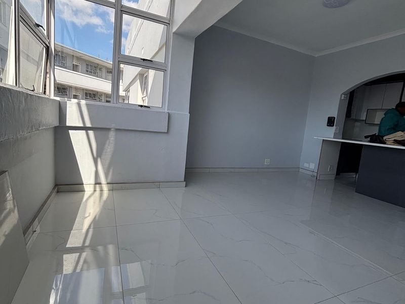 Bright and spacious open-plan living area featuring modern porcelain tile flooring, large windows providing natural light, and a convenient breakfast bar.