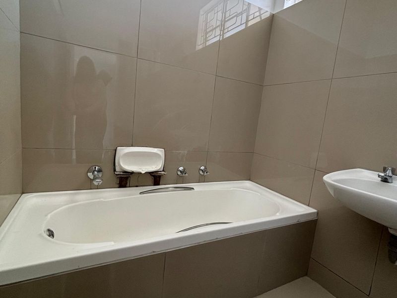 A functional bathroom featuring a built-in bathtub, wall-mounted basin, and neutral ceramic tiling throughout.
