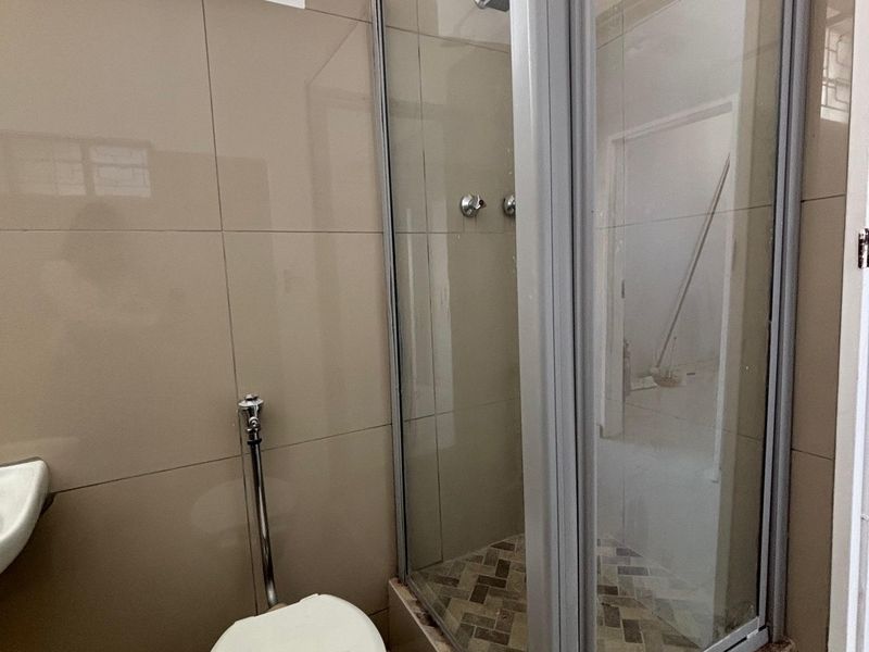 A functional bathroom featuring a glass-enclosed shower, toilet, and neutral wall tiling. The space is currently vacant and ready for updates.