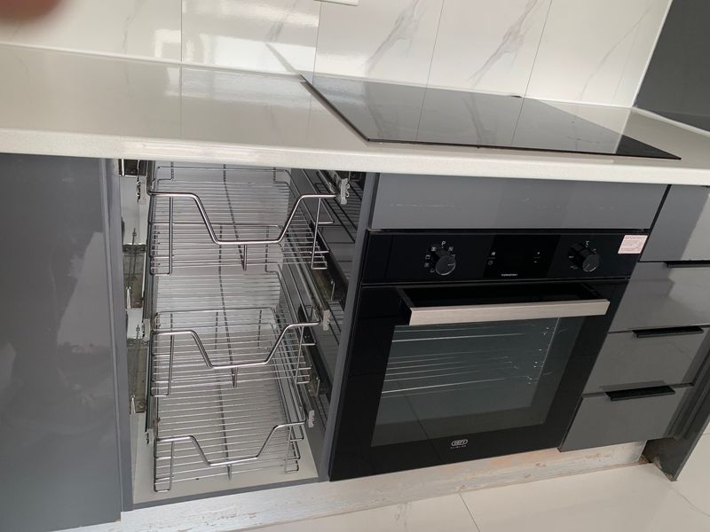 Modern kitchen featuring a built-in oven, induction hob, stone countertops, and a convenient pull-out wire pantry unit with sleek glossy cabinetry.