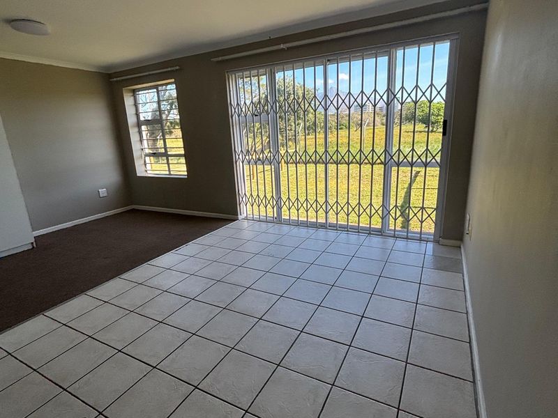 An empty living room featuring a mix of tiled and carpeted flooring, with a sliding glass door leading to an outdoor area.