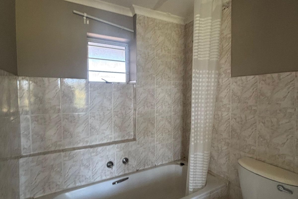A dated bathroom featuring a built-in bathtub, toilet, and tiled finishes, currently requiring ceiling repairs and cosmetic updates.