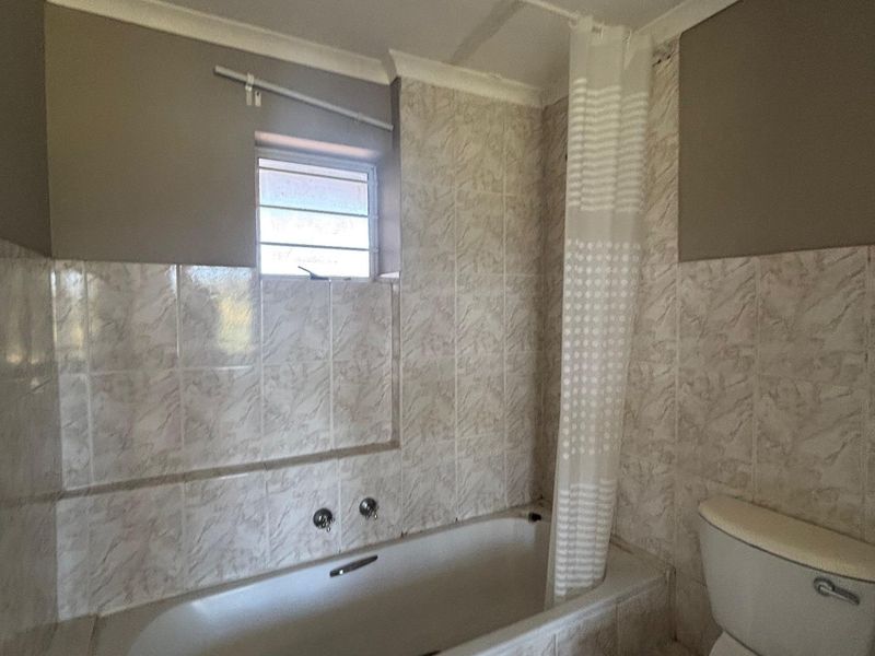 A dated bathroom featuring a built-in bathtub, toilet, and tiled finishes, currently requiring ceiling repairs and cosmetic updates.