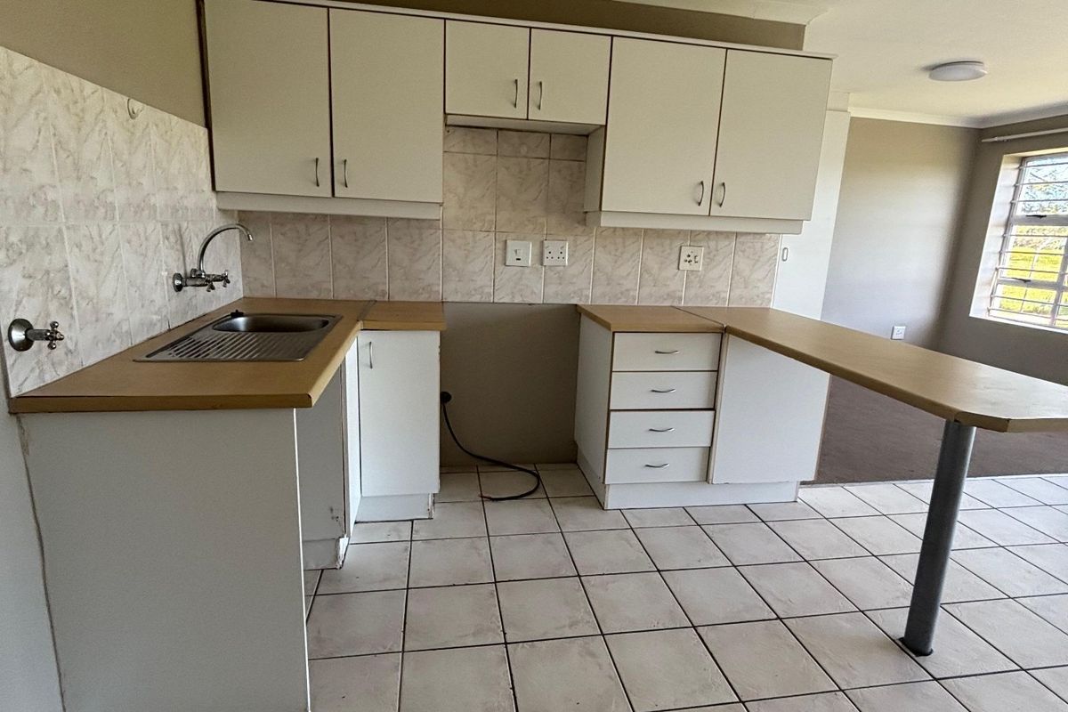 A functional kitchen featuring white cabinetry, laminate countertops, a breakfast bar, and tiled flooring, offering a clean and practical layout for daily use.