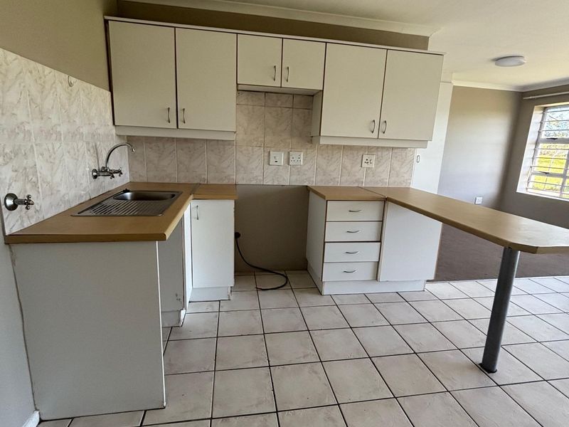 A functional kitchen featuring white cabinetry, laminate countertops, a breakfast bar, and tiled flooring, offering a clean and practical layout for daily use.
