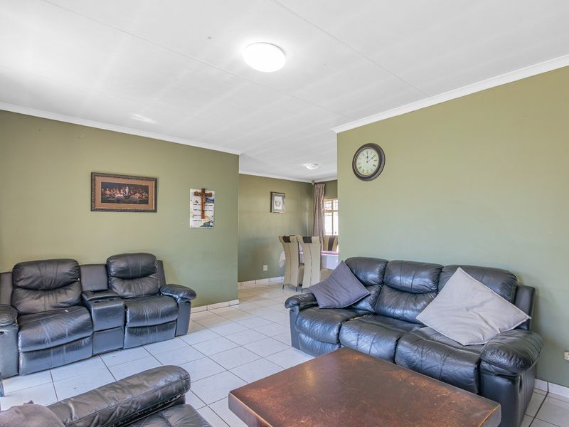 Open plan living and dining area featuring tiled flooring and neutral green walls, providing a functional space for family gatherings.