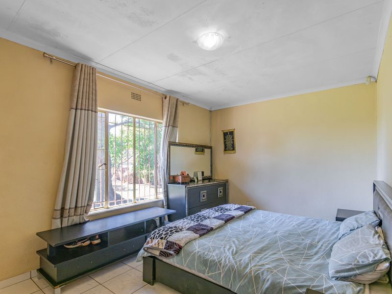 A bedroom featuring tiled flooring and a window with security bars. The room requires cosmetic updates to the ceiling and wall finishes.