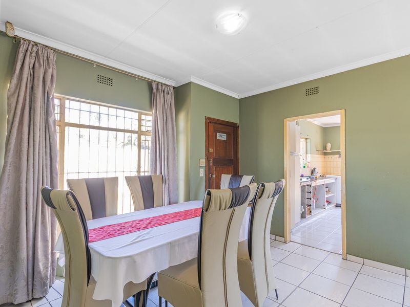 Dining room featuring tiled flooring, large window with security bars, and direct access to the adjacent kitchen area.