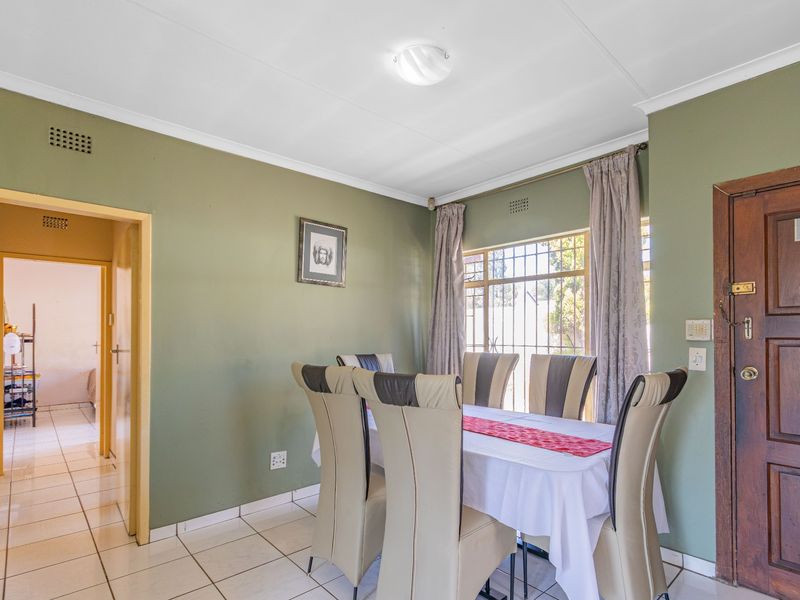 A dining room featuring tiled flooring, a wooden entrance door, and security bars on the window, providing a functional space for family meals.