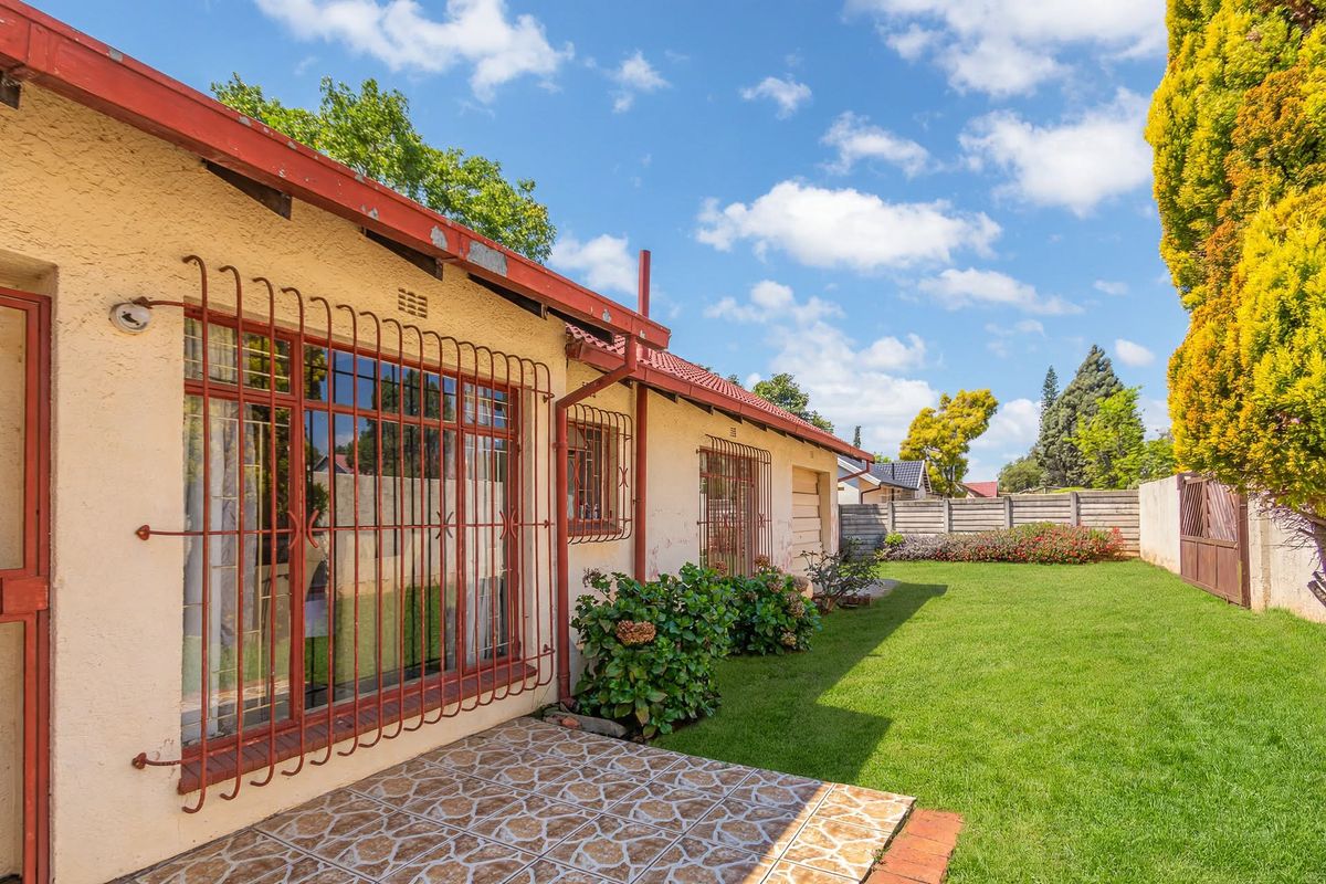 Rear view of the house featuring a tiled patio, security bars on windows, and a well-maintained lawn with perimeter walling.