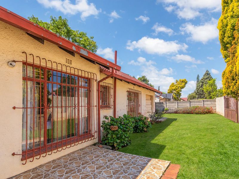 Rear view of the house featuring a tiled patio, security bars on windows, and a well-maintained lawn with perimeter walling.