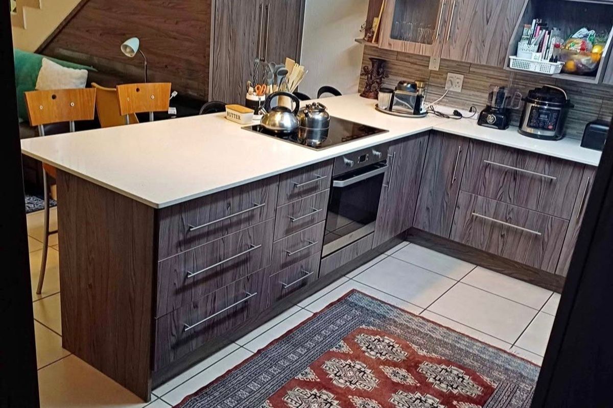 Modern kitchen featuring wood-grain cabinetry, stone countertops, integrated electric hob and oven, and tiled flooring, conveniently located adjacent to the staircase.
