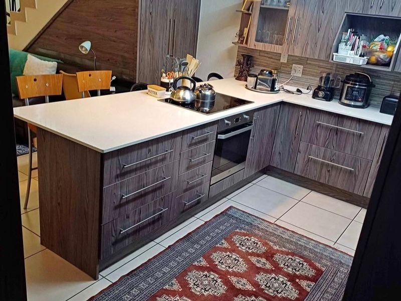 Modern kitchen featuring wood-grain cabinetry, stone countertops, integrated electric hob and oven, and tiled flooring, conveniently located adjacent to the staircase.