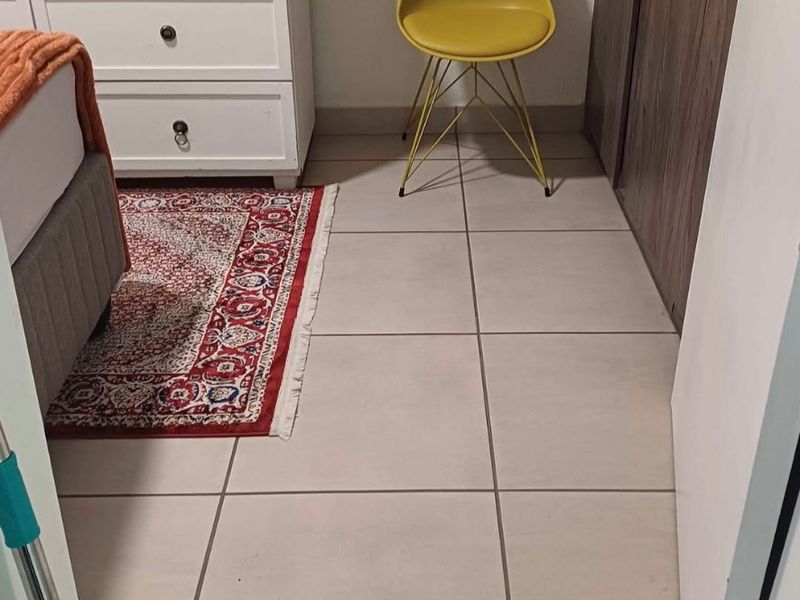 A bedroom interior featuring neutral ceramic floor tiles and a built-in wooden wardrobe.