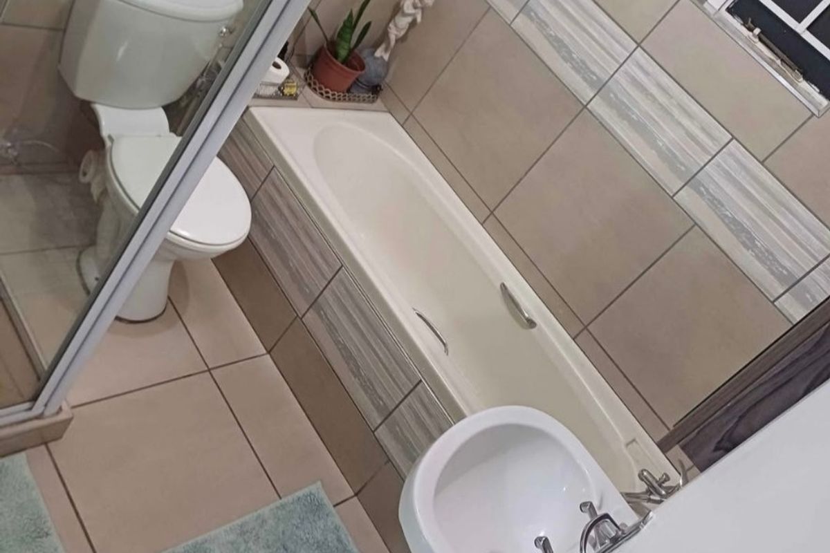 A functional bathroom featuring a bathtub, separate shower enclosure, pedestal basin, and neutral wall tiling.