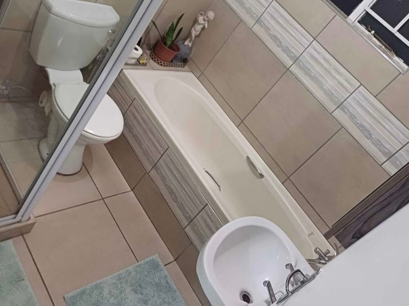 A functional bathroom featuring a bathtub, separate shower enclosure, pedestal basin, and neutral wall tiling.