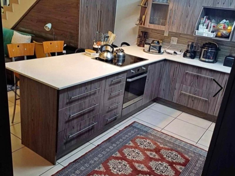 Modern kitchen featuring wood-grain cabinetry, stone countertops, integrated electric hob and oven, and pendant lighting, situated adjacent to an internal staircase.