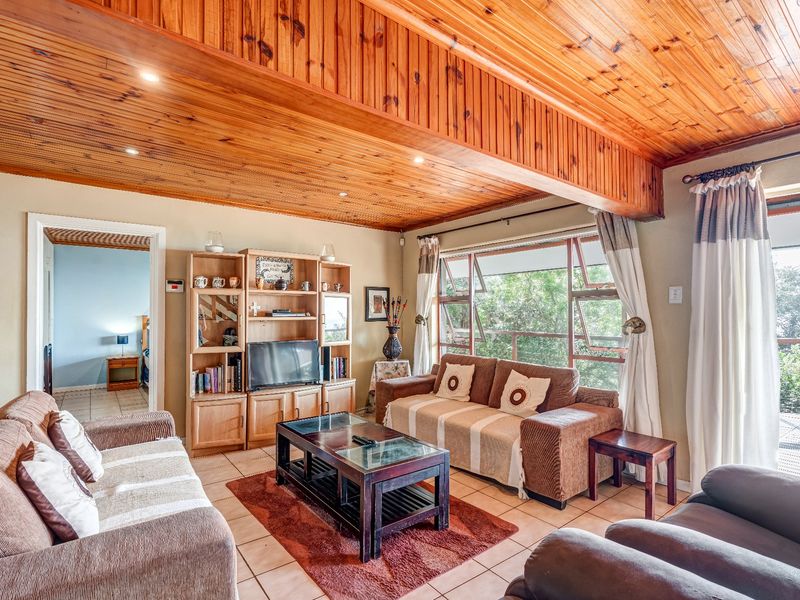 Spacious living room featuring a warm timber tongue and groove ceiling, tiled flooring, and large windows providing natural light and garden views.