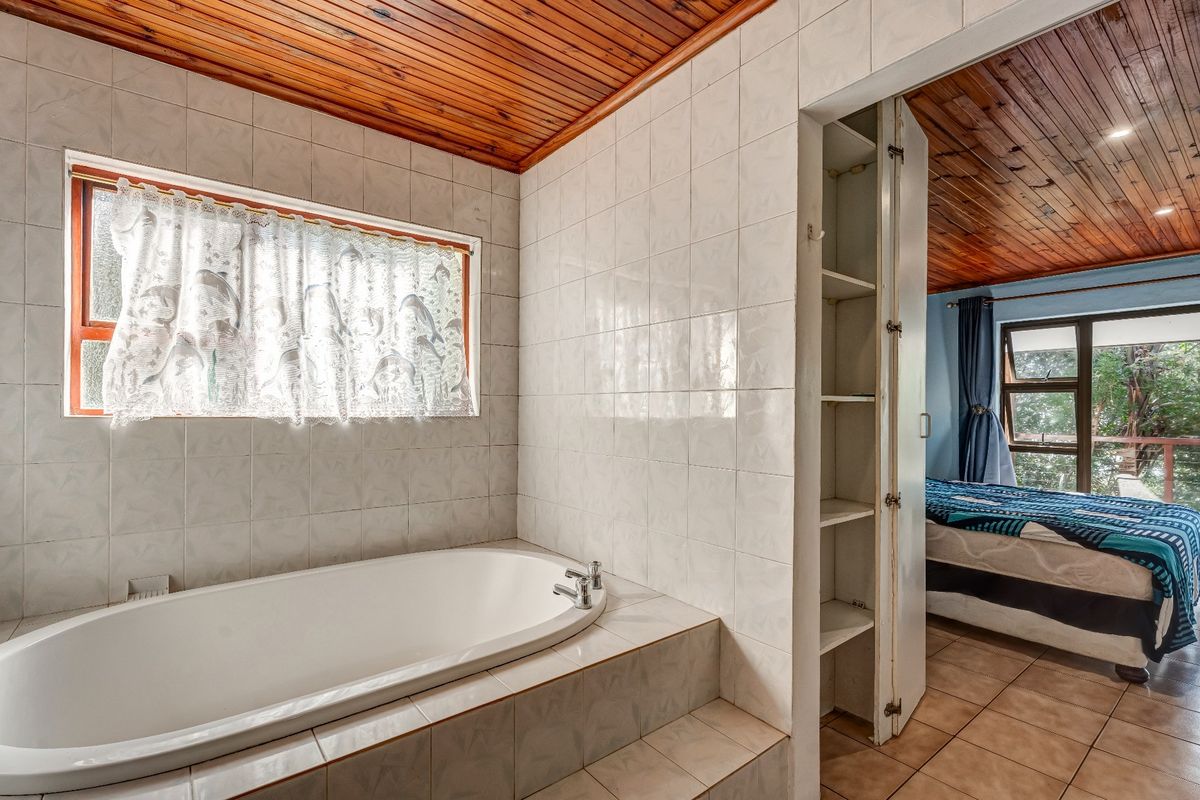 A bathroom featuring a built-in bathtub, tiled walls, and a timber ceiling, with an adjacent built-in storage cupboard and tiled flooring.