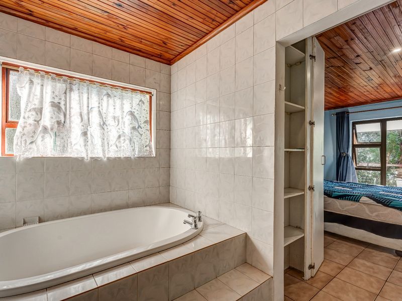 A bathroom featuring a built-in bathtub, tiled walls, and a timber ceiling, with an adjacent built-in storage cupboard and tiled flooring.