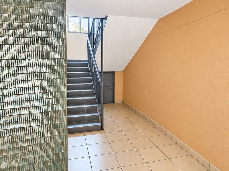 A clean, well-maintained apartment hallway featuring tiled flooring, a staircase with a metal handrail, and a decorative mosaic feature wall.