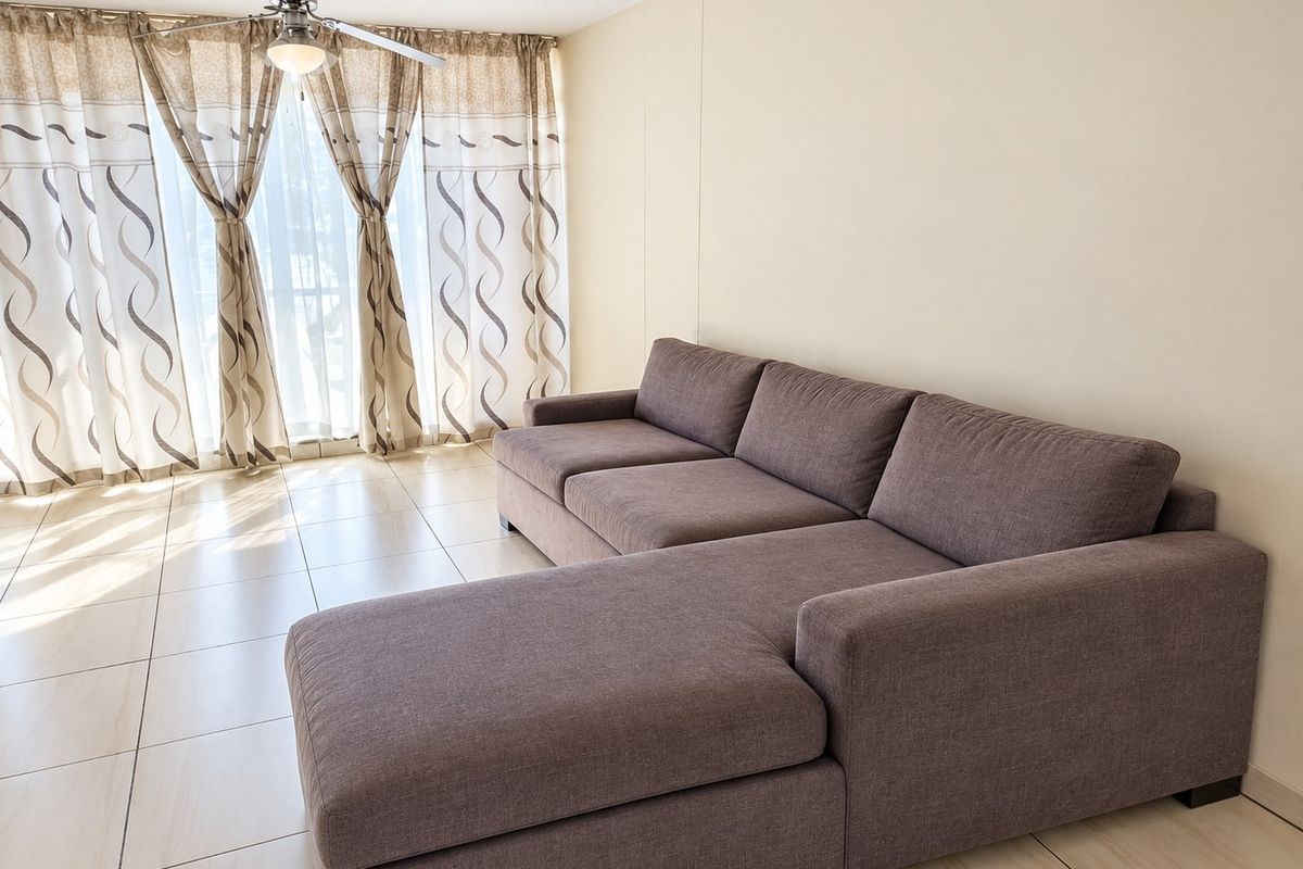 A bright living room featuring neutral tiled flooring, a ceiling fan, and large sliding glass doors that provide ample natural light.