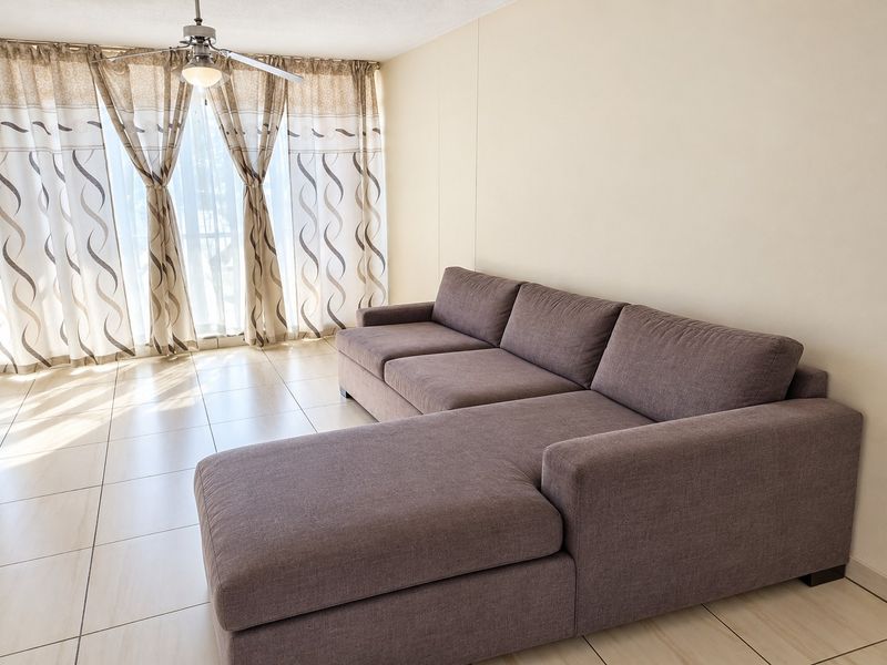 A bright living room featuring neutral tiled flooring, a ceiling fan, and large sliding glass doors that provide ample natural light.
