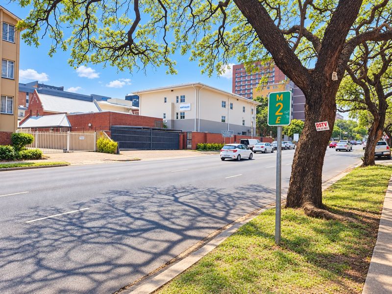 A street-level view showing the exterior facade, perimeter wall, and security access gate of the apartment complex.
