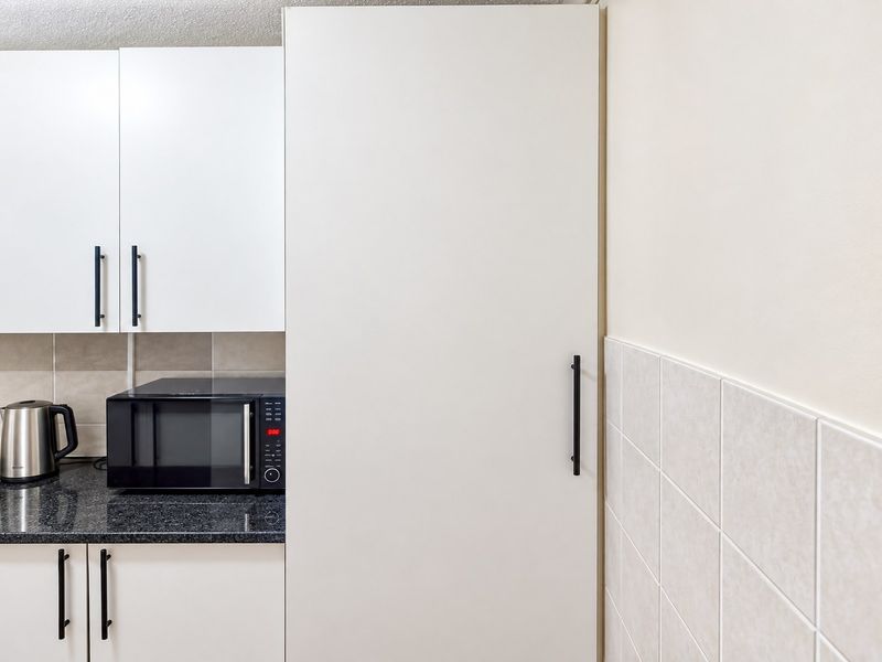 A clean, modern kitchen area featuring white cabinetry, a dark granite-effect countertop, and neutral tiled backsplash with a built-in microwave.