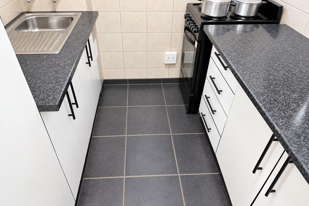 A compact, functional kitchen featuring white cabinetry, dark laminate countertops, a stainless steel sink, and a freestanding stove with tiled splashbacks.