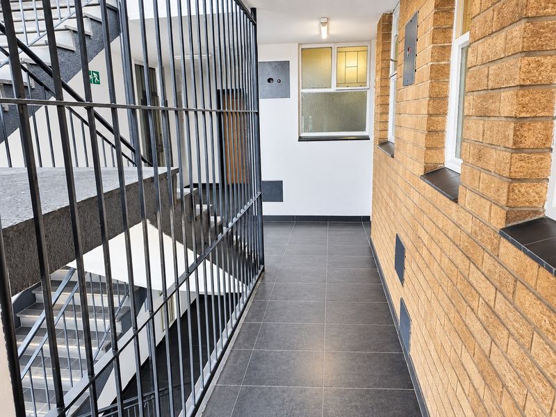 A clean, well-maintained apartment building hallway featuring tiled flooring, brick wall accents, and a secure metal staircase railing.