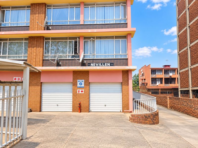 Front elevation of the Nevillen apartment complex featuring brick facade, paved driveway access, and secure roller garage doors.