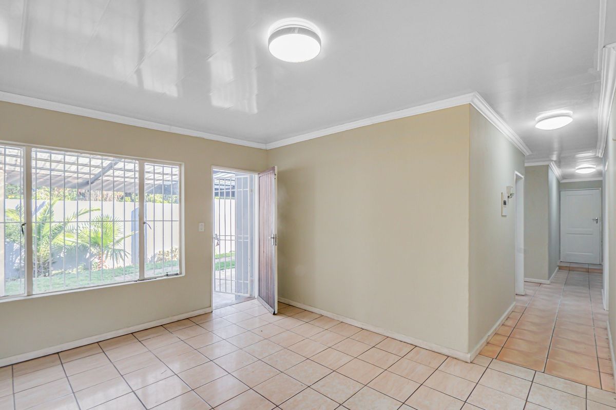 A bright, empty living area featuring neutral walls, tiled flooring, and direct access to the exterior through a secure door.