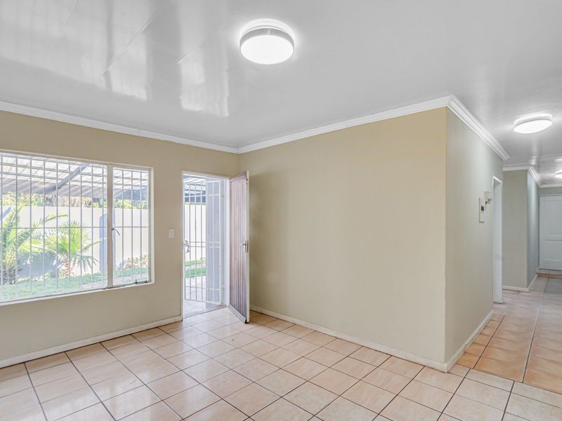 A bright, empty living area featuring neutral walls, tiled flooring, and direct access to the exterior through a secure door.